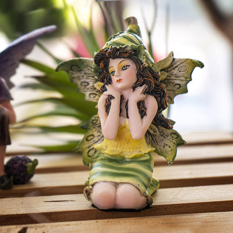 Figurine of sitting fairy in green and yellow dress with matching wings and hat, brown hair, yellow-brown eyes