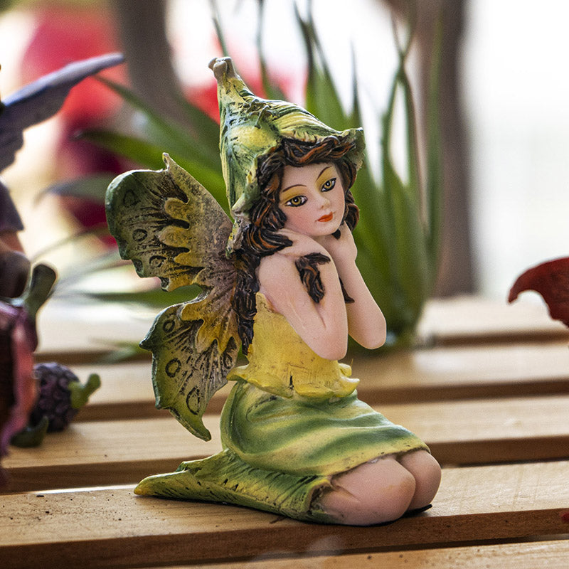 Figurine of sitting fairy in green and yellow dress with matching wings and hat, brown hair, yellow-brown eyes