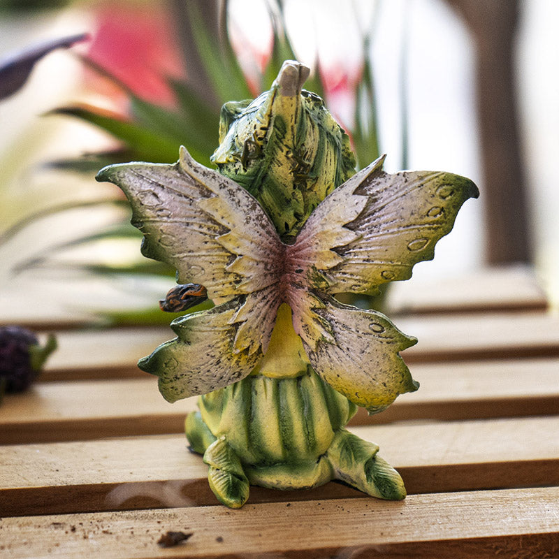 Figurine of sitting fairy in green and yellow dress with matching wings and hat, brown hair, yellow-brown eyes, shown from the back