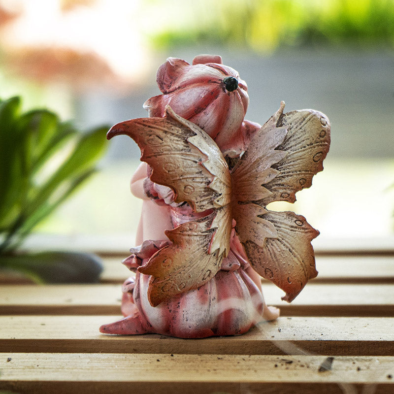 Fairy figurine, pink dress, wings and flower hat. Blond-streaked brown hair with golden yellow-brown eyes. Shown from the back