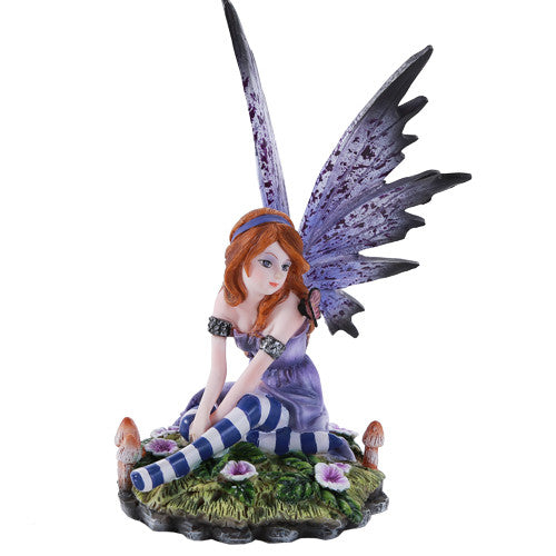 Figurine of fairy sitting on grass with flowers and mushrooms. Indigo dress and wings, striped stockings, red hair, gazing off to the side