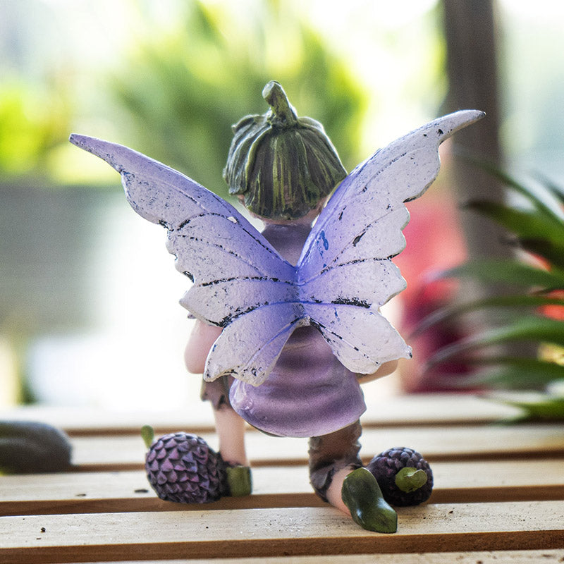 Fairy boy figurine with purple wings, green flower bud hat, holding a berry with more berries next to him. Shown from the back