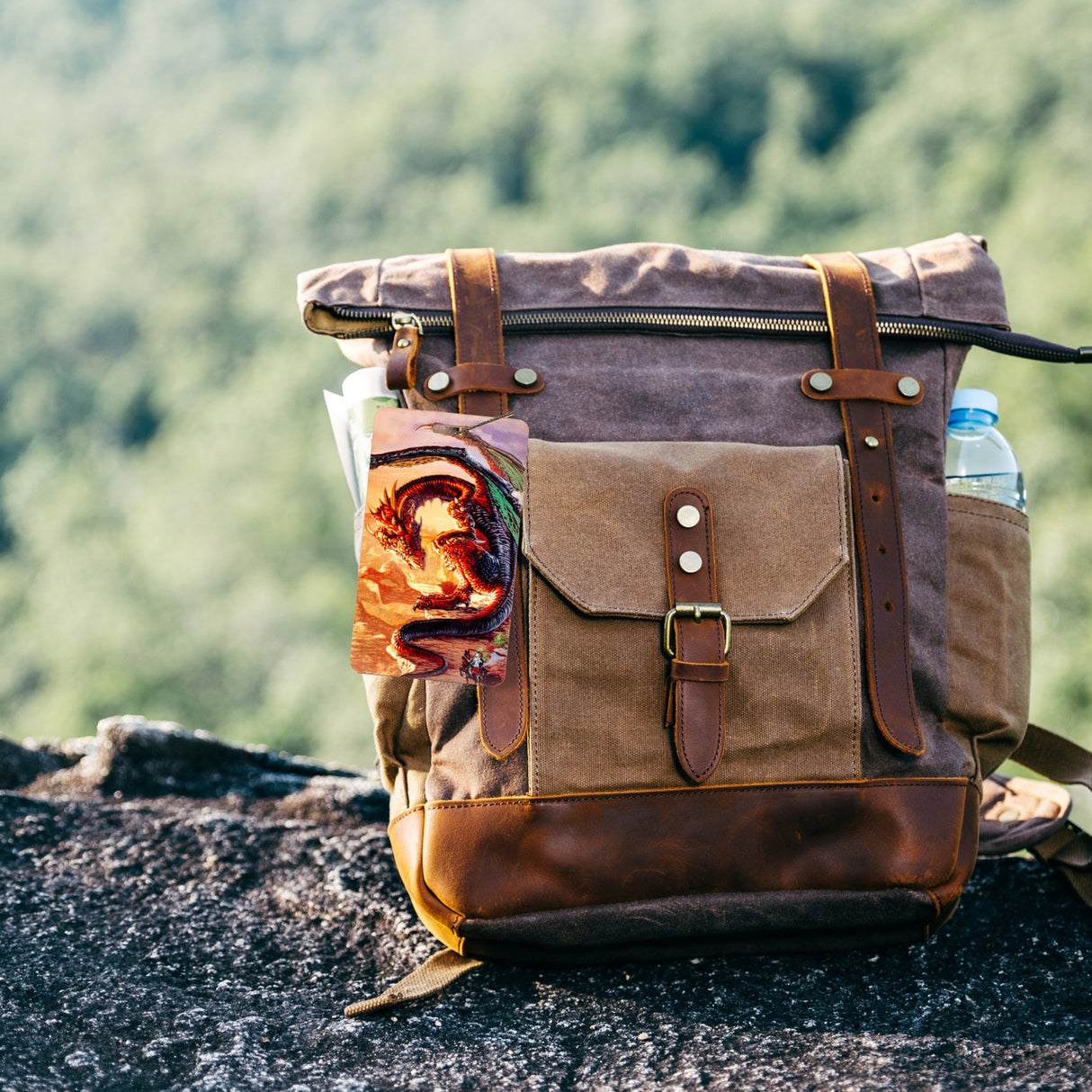Luggage tag with a dragon and knight design shown attached to a brown leather backack out in nature