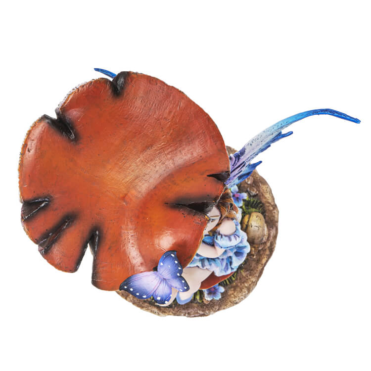 The statue shows a fairy sitting on a toadstool. She wears a dress of ruffled blue, and has indigo wings to match. A butterfly perches on her hand, and another purple flutterby sits on a taller mushroom.