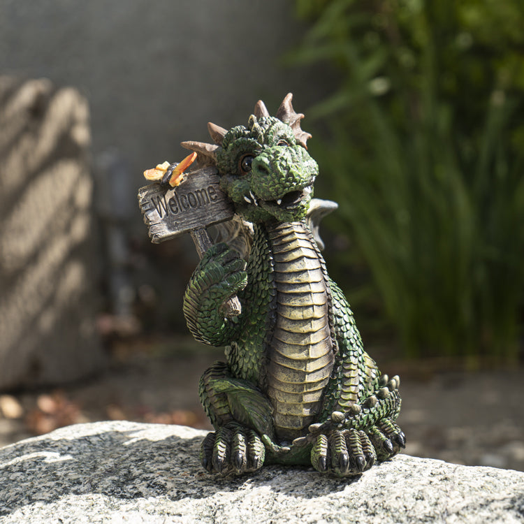 Dragon statue holding a 'Welcome' sign. Dragon is green with brown accents, yellow butterfly on the sign.