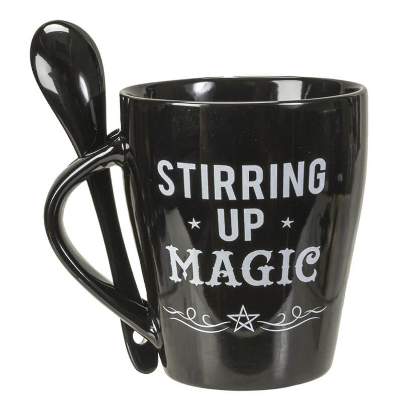 Coffee mug in black with "STIRRING UP MAGIC" text and stars, spoon slots into handle and has a pentacle
