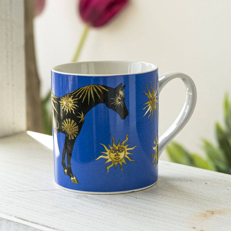 A blue ceramic mug featuring a black horse decorated with gold sun & moon motifs