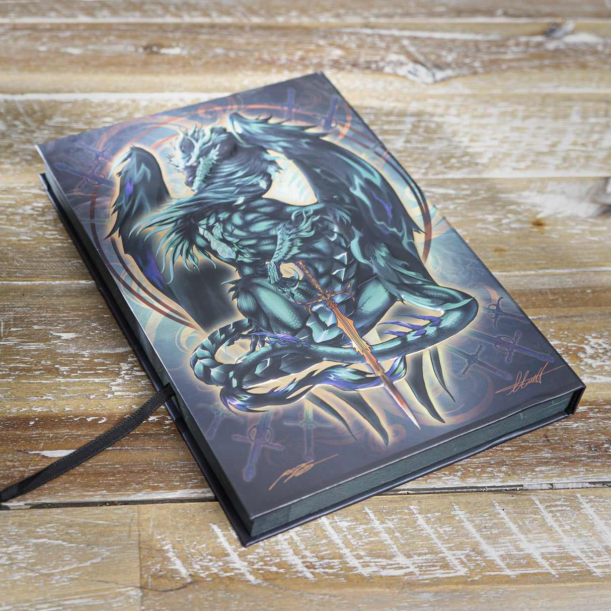 Journal with cover art of green-gray dragon and sword, more weapons and swirls behind
