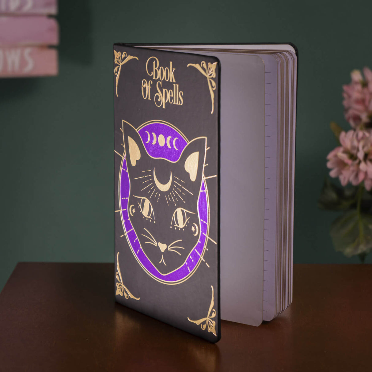 Black journal with purple and gold designs, black cat with celestial accents and "Book of Spells" written
