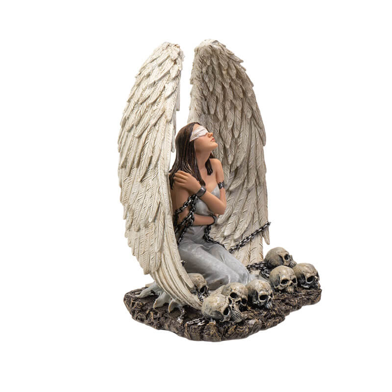 Figurine of a white winged angel woman in chains, blindfolded sitting amongst skulls
