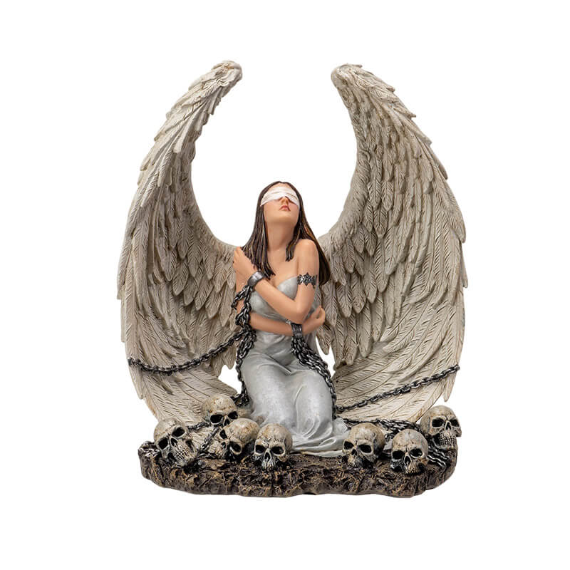 Figurine of a white winged angel woman in chains, blindfolded sitting amongst skulls
