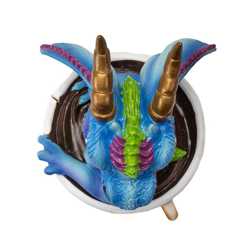 Figurine of blue, purple, green dragon with gold horns sitting in a cup of tea. Top down