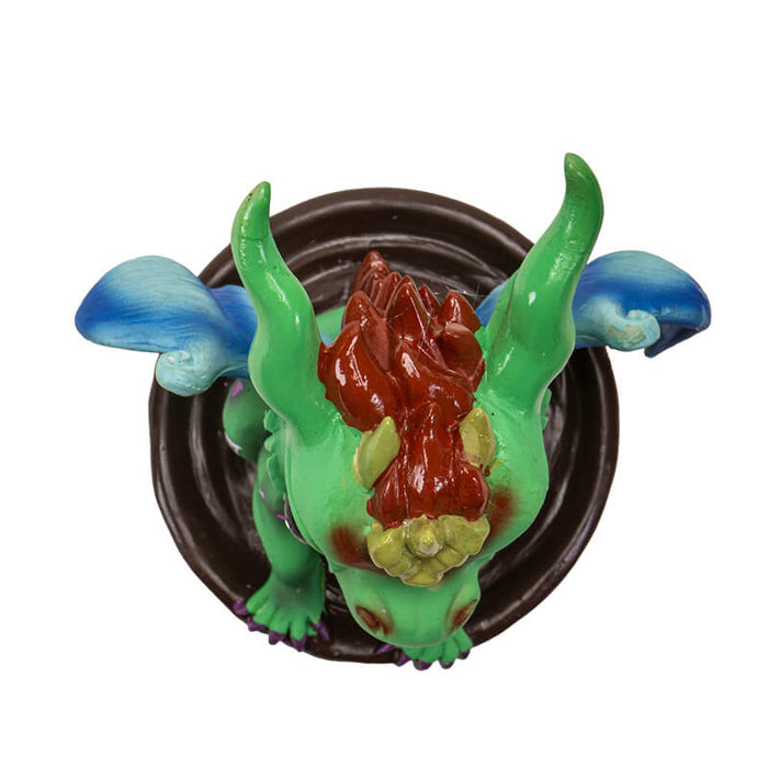 Figurine of a green dragon with blue wings and gold and red accents in a mug of chai. Top down view