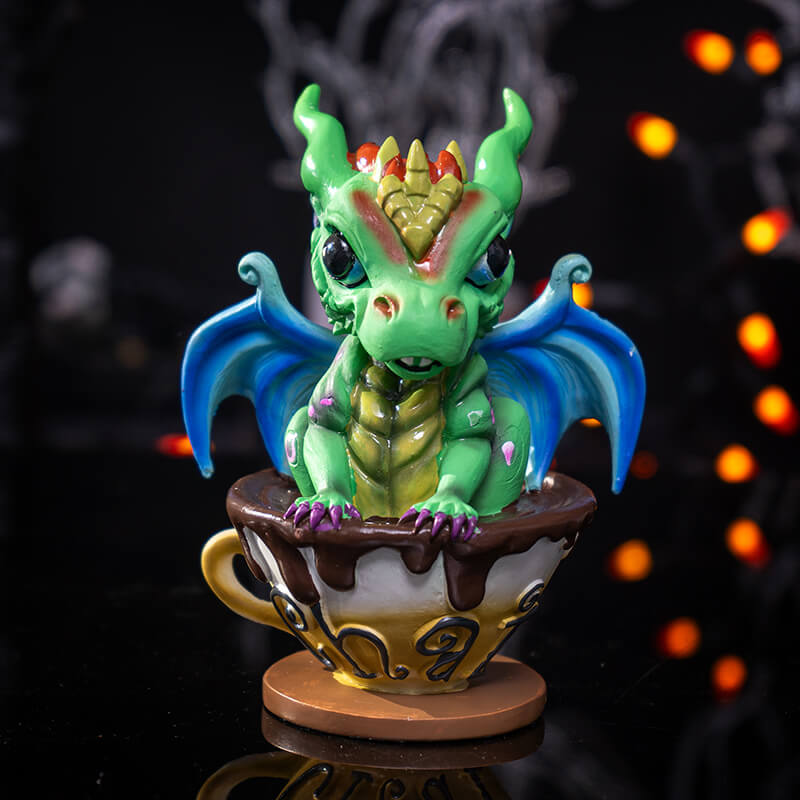 Figurine of a green dragon with blue wings and gold and red accents in a mug of chai.