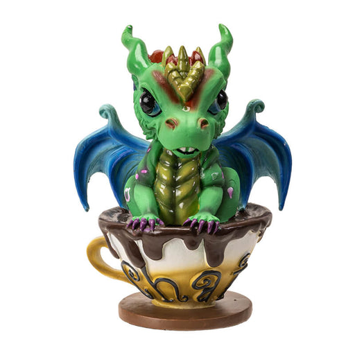 Figurine of a green dragon with blue wings and gold and red accents in a mug of chai.