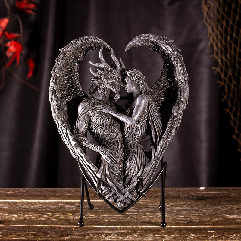 Figurine on stand of demon and angel forming a heart with their wings, done in faux-stone.