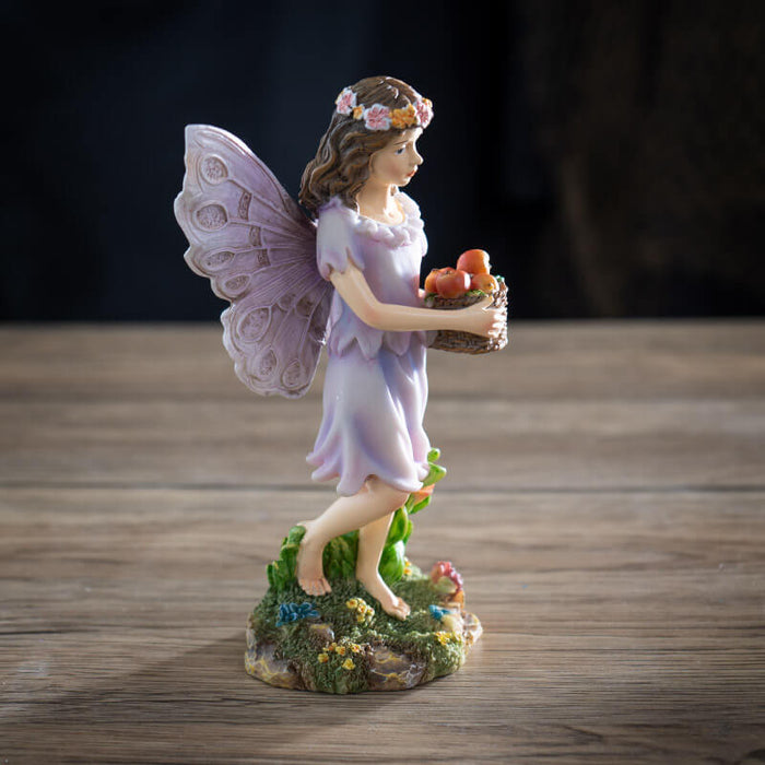 Figurine of a fairy with brown hair and flower crown carrying a basket of apples.