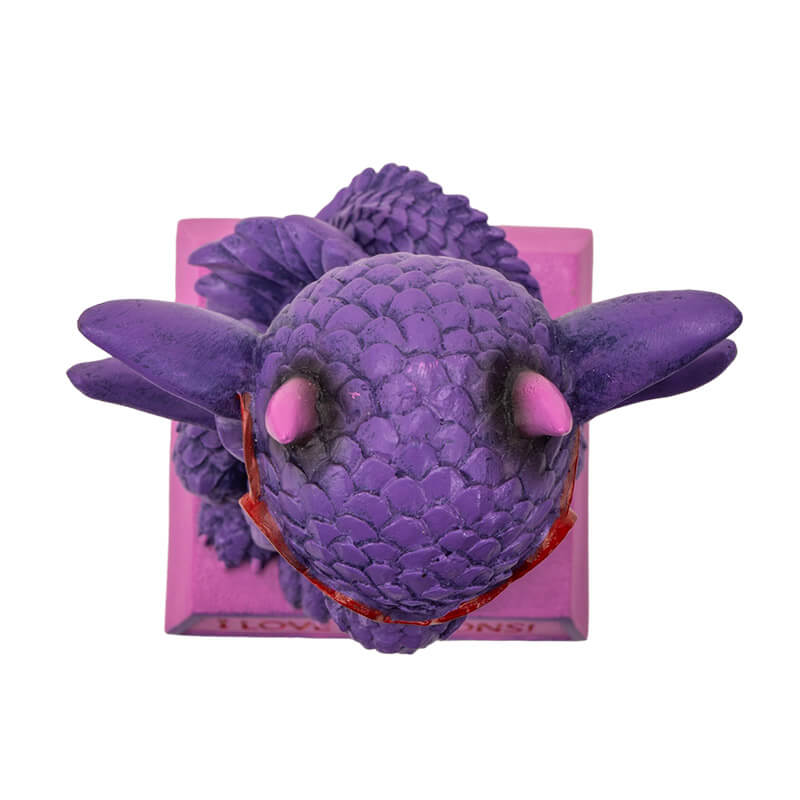 Figurine of a dragon sitting on a pink base that says "I LOVE DRAGONS!" The dragon is purple and pink with red heart glasses and a little burst of fire. Shown top down