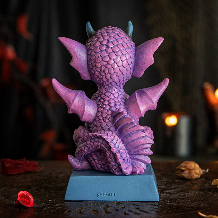 Figurine of a pink dragon with blue tummy and horns and a flame, sitting on indigo base that reads "She's cute but fierce!" Back view