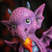 Figurine of a pink dragon with blue tummy and horns and a flame, sitting on indigo base that reads "She's cute but fierce!"