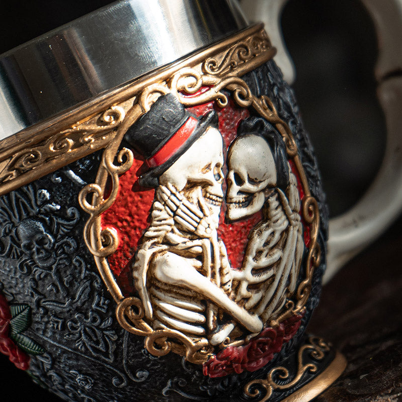 Teacup with stainless steel insert. Skeleton couple embraces against a black background with gold accents and red roses. Faux-bone handle.