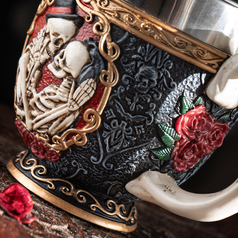 Teacup with stainless steel insert. Skeleton couple embraces against a black background with gold accents and red roses. Faux-bone handle.