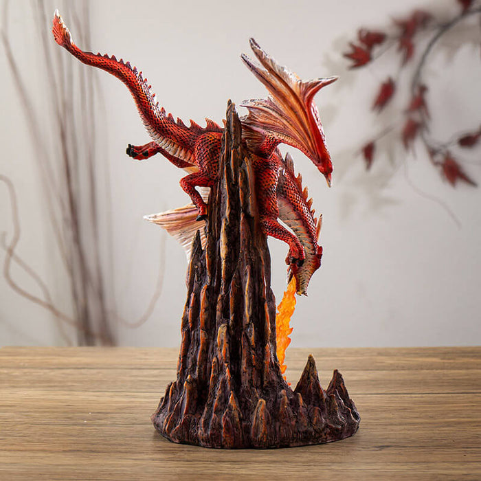 Figurine of a red dragon flying over rocks, breathing a column of orange fire