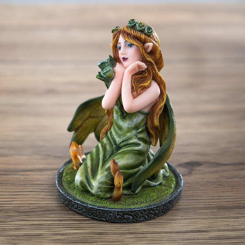 Figurine of small fairy with crystals and mushrooms where she kneels in the moss, holding a bouquet of flowers with more in her blond hair.