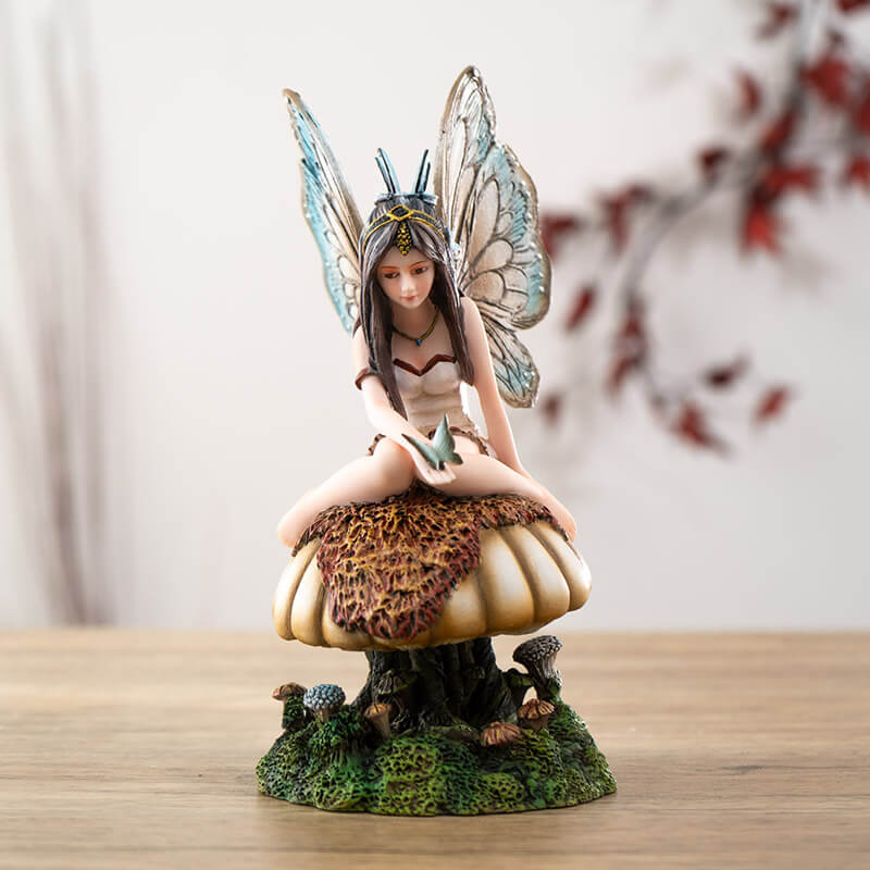 Figurine of brunette fairy with tan and brown wings and cream dress sitting on mushroom with butterfly on her hand, more toadstools below.