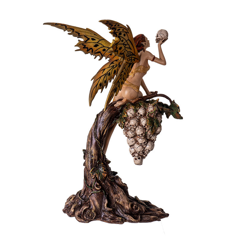 Figurine of fairy in tan garb with tan and black wings holding skull, perched on grapevine of more skulls