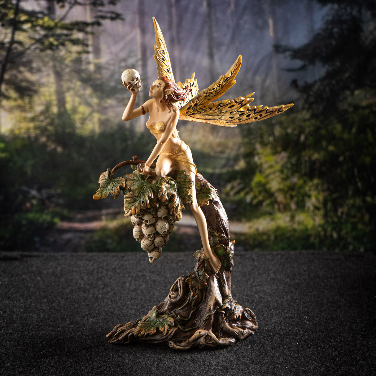 Figurine of fairy in tan garb with tan and black wings holding skull, perched on grapevine of more skulls