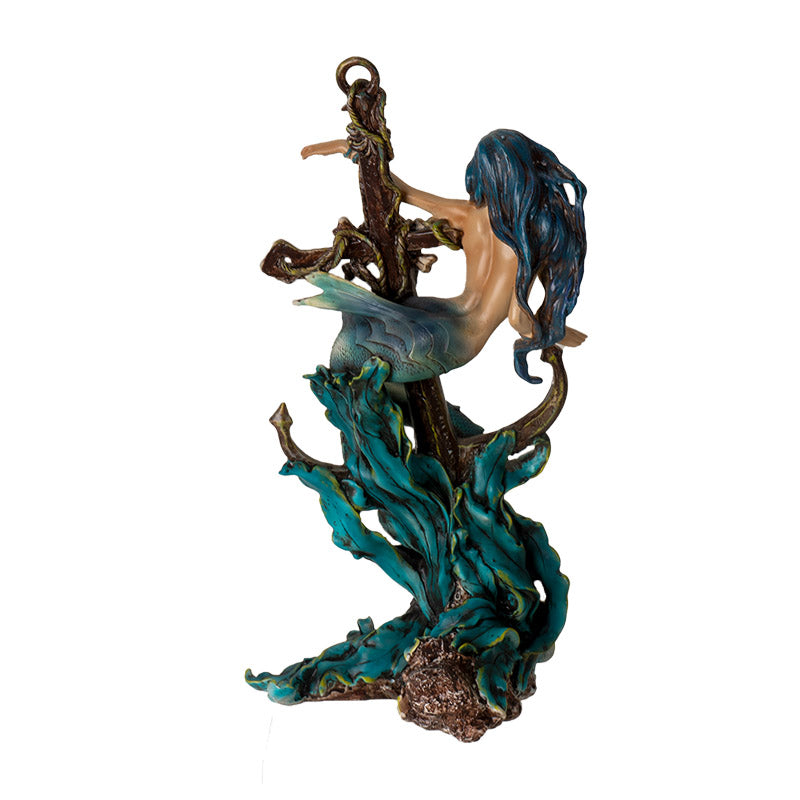 Figurine of a mermaid wrapped around an anchor with a skeleton and seaweed, shown from the back, she has blue hair