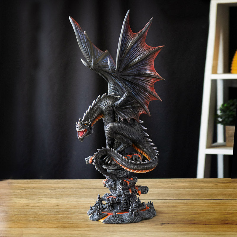 Figurine of a black dragon with blue, red, orange accents, perched snarling on a rocks with lava