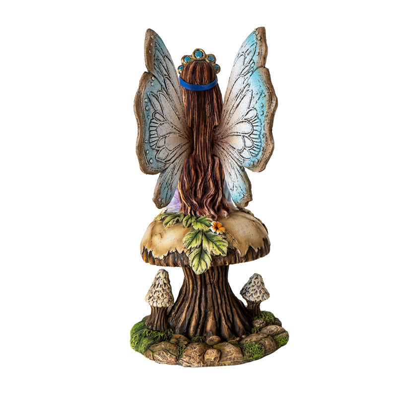 Figurine of a brunette fairy with blue tinged wings and dress sitting on tan mushroom with flowers and leaves, holding baby blue dragon in egg in one palm, shown from the back