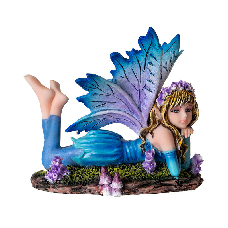 Fairy figurine - pixie laying down, wearing blue dress with leggings and feet kicked up behind her. Blue wings, purple flower and mushroom accents