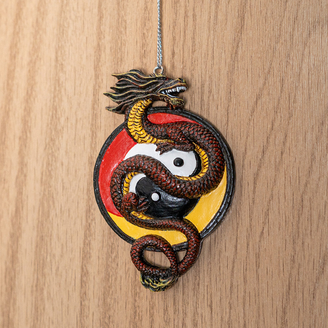 Ornament of red-brown Asian dragon with yellow belly curled around white and black yin yang circle on a red and yellow background