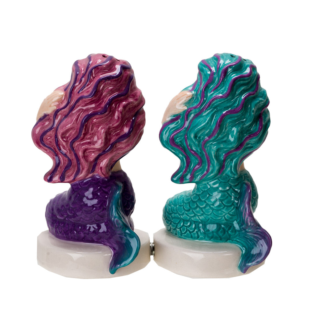 Salt and pepper shakers shaped like mermaids. One in teal with purple and gold accents, one in purple with pink and teal accents, shown from the back