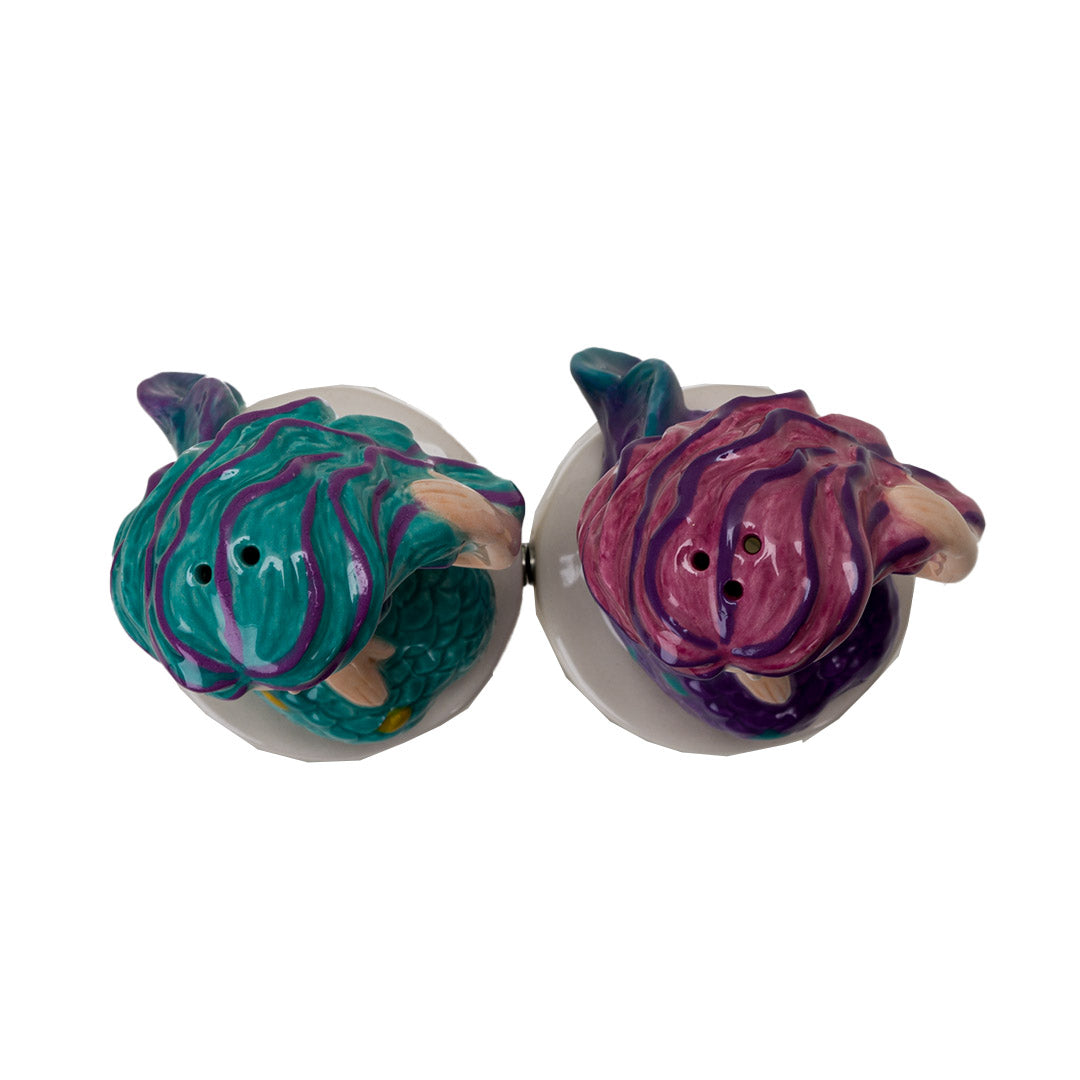 Salt and pepper shakers shaped like mermaids. One in teal with purple and gold accents, one in purple with pink and teal accents, shown top down