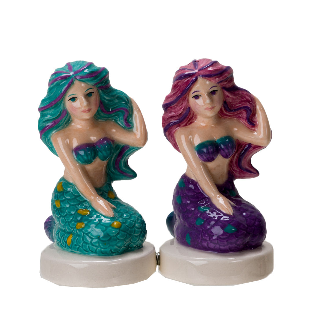 Salt and pepper shakers shaped like mermaids. One in teal with purple and gold accents, one in purple with pink and teal accents