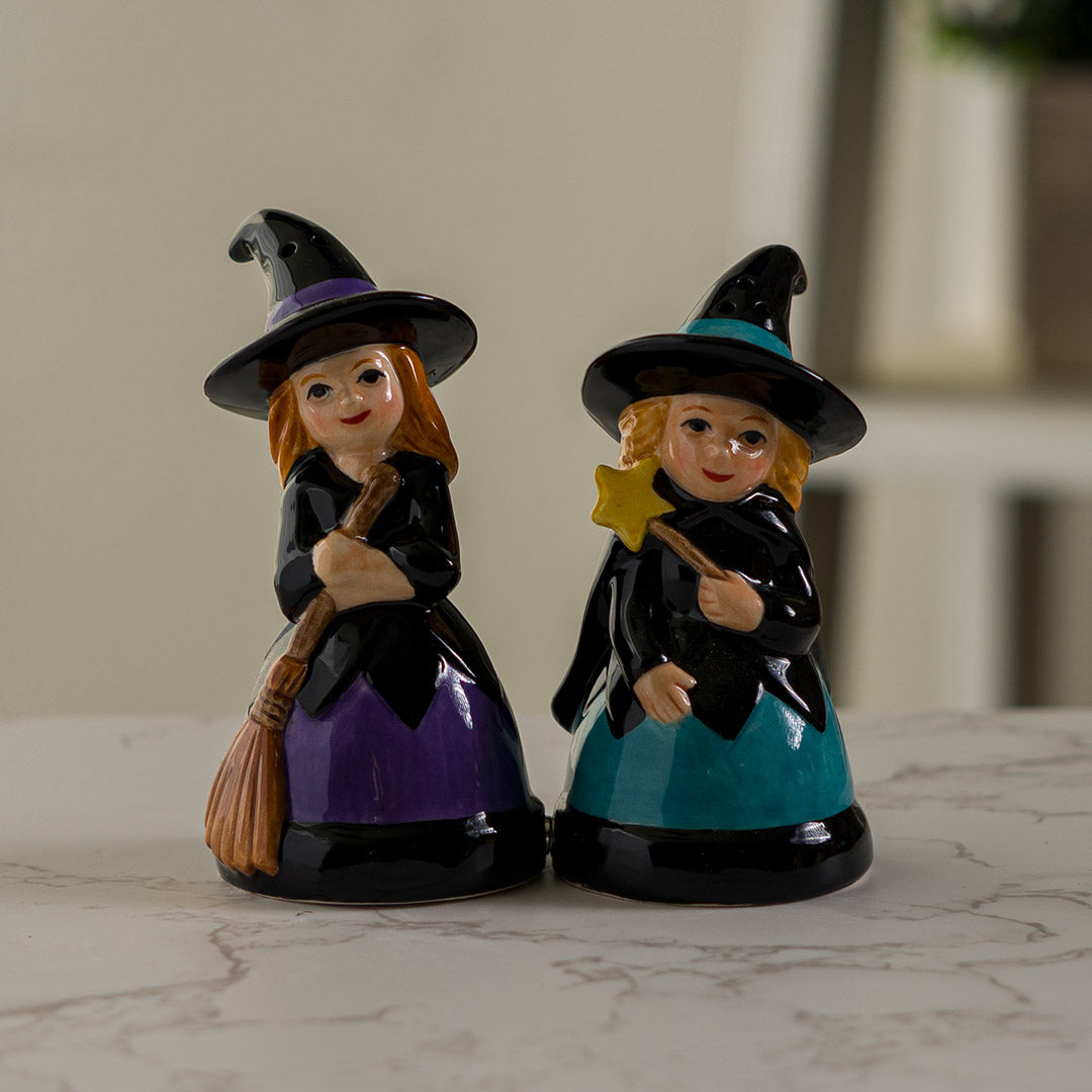 Salt & Pepper shakers shaped like witches in black hats and dresses. One accented in purple holding a broom, the other with blue accents holding a star wand