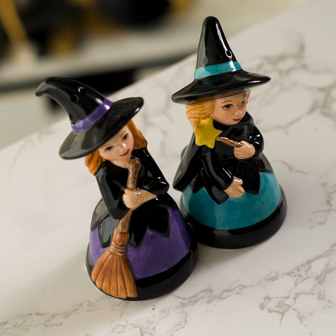 Salt & Pepper shakers shaped like witches in black hats and dresses. One accented in purple holding a broom, the other with blue accents holding a star wand