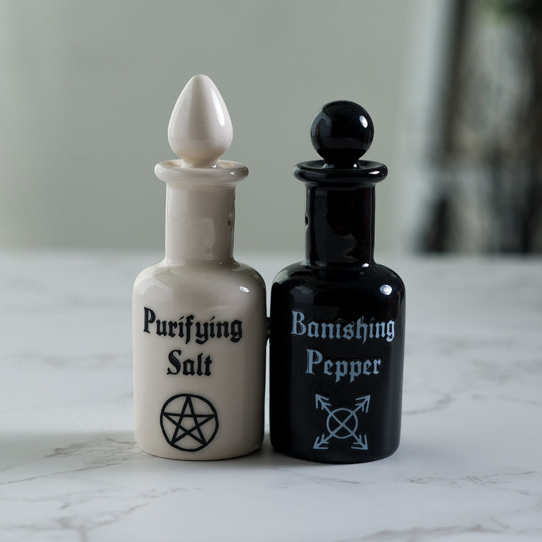 Salt and pepper shakers shaped like potion bottles. White one reads "Purifying Salt" and black one has "Banishing Pepper" with arcane symbols, attached via magnets to one another