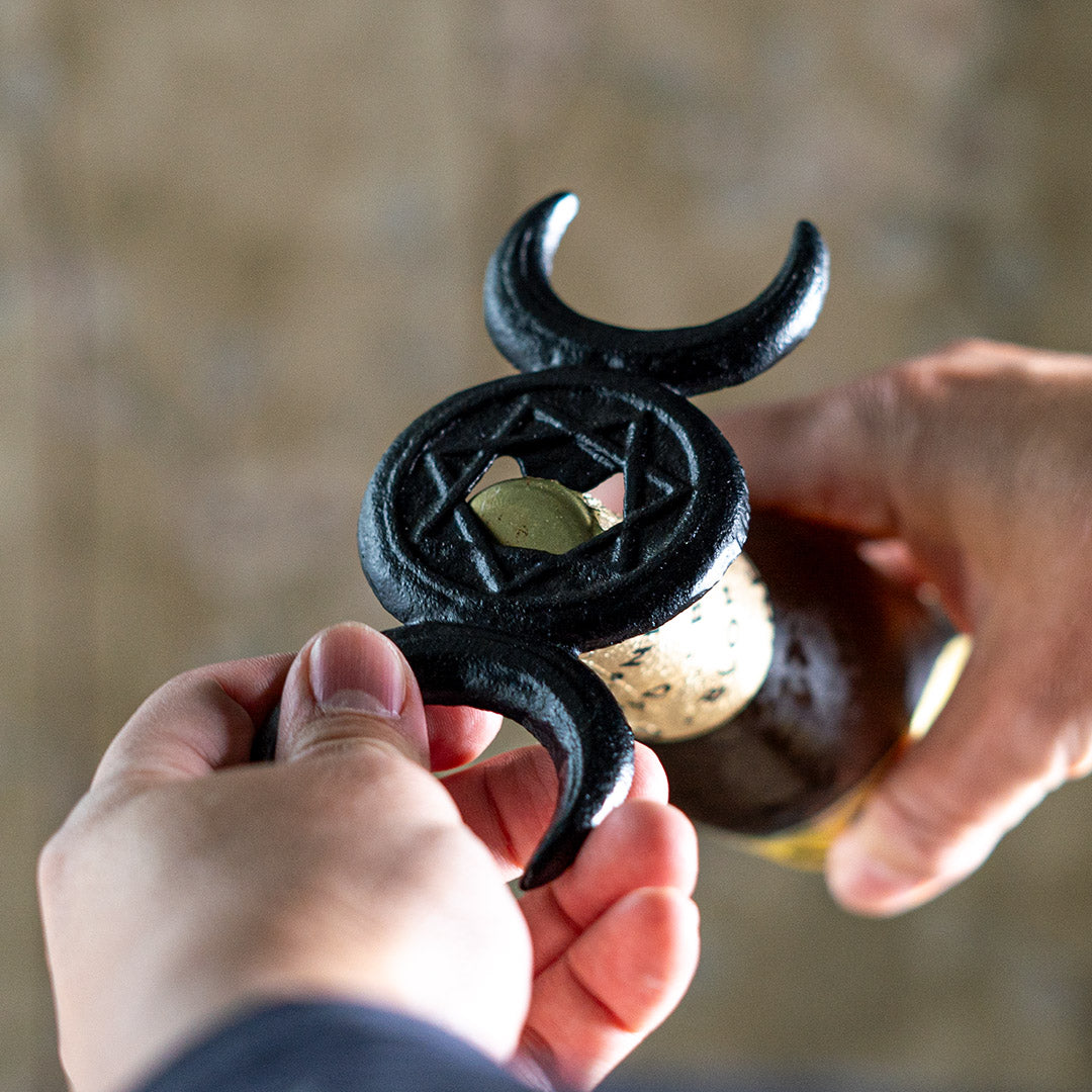 Cast iron black triple moon bottle opener, shown opening a bottle