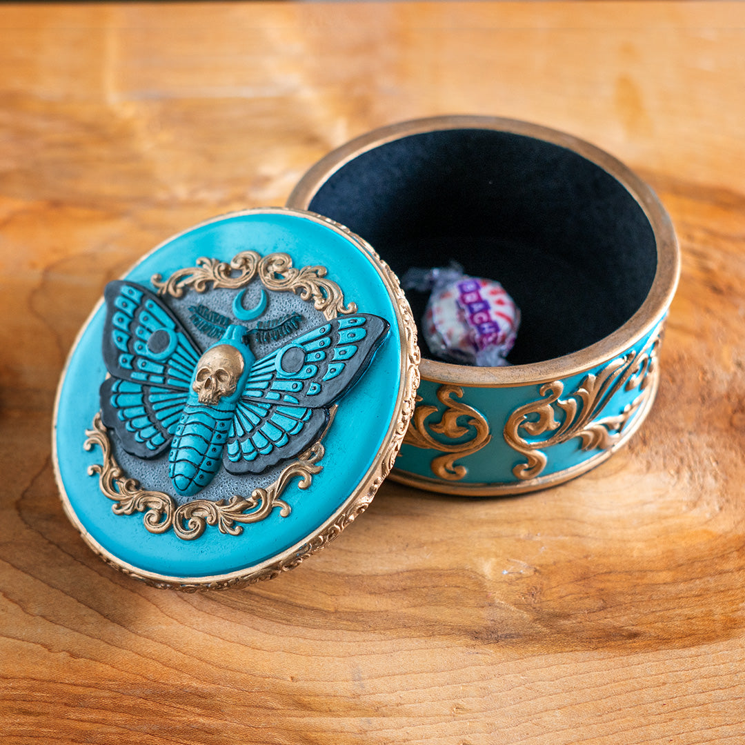 Round trinket box with blue base and moth design, gold accents, skull and swirls