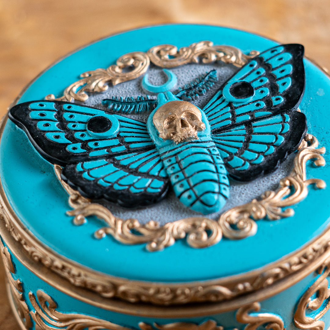 Round trinket box with blue base and moth design, gold accents, skull and swirls