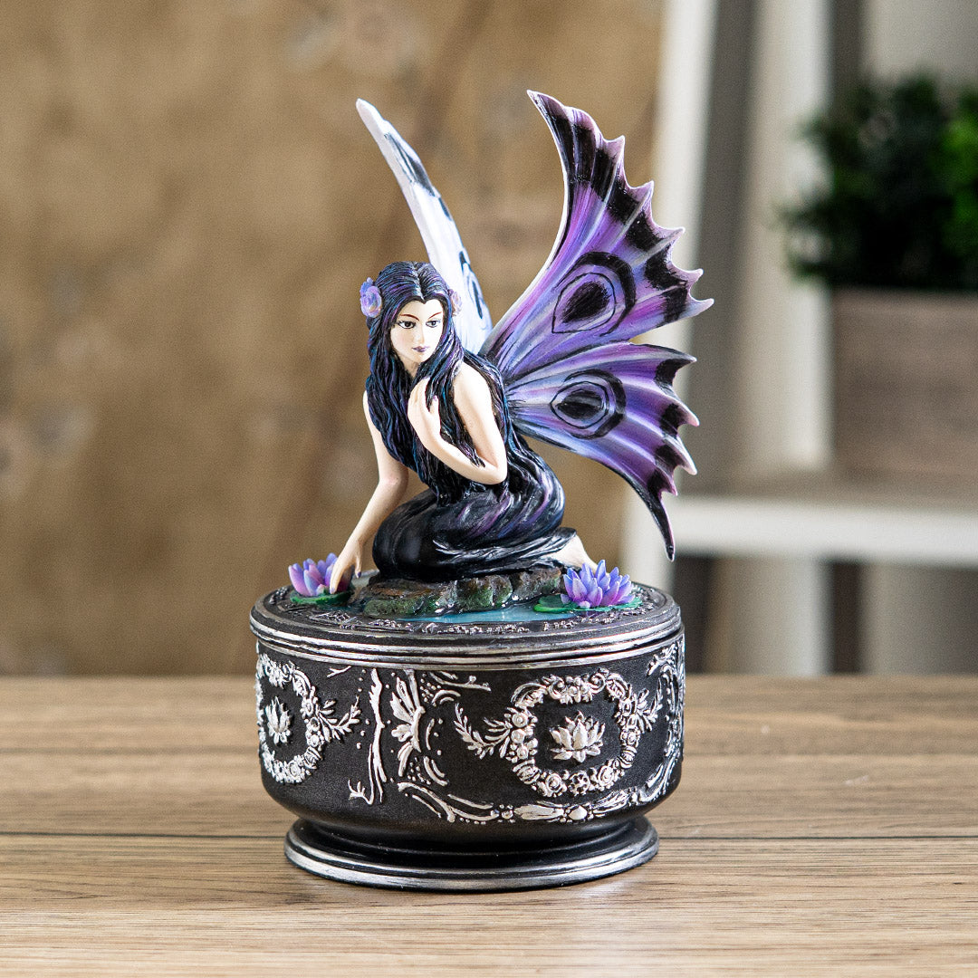 Trinket box with black base and silver designs. On the lid is a fairy in black dress with purple and blue wings accented in black, sitting amidst water lilies