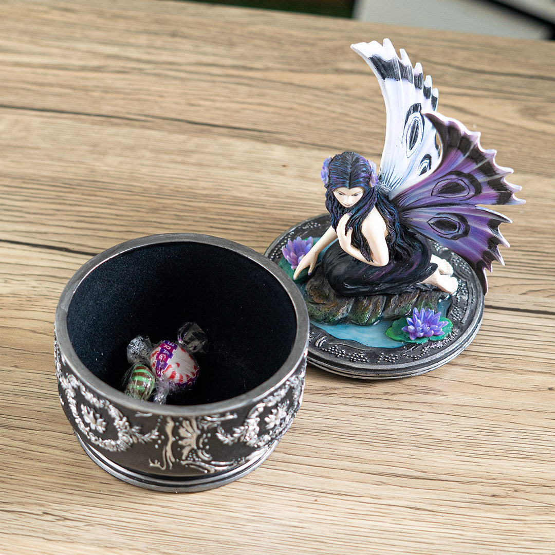 Trinket box with black base and silver designs. On the lid is a fairy in black dress with purple and blue wings accented in black, sitting amidst water lilies. Shown open