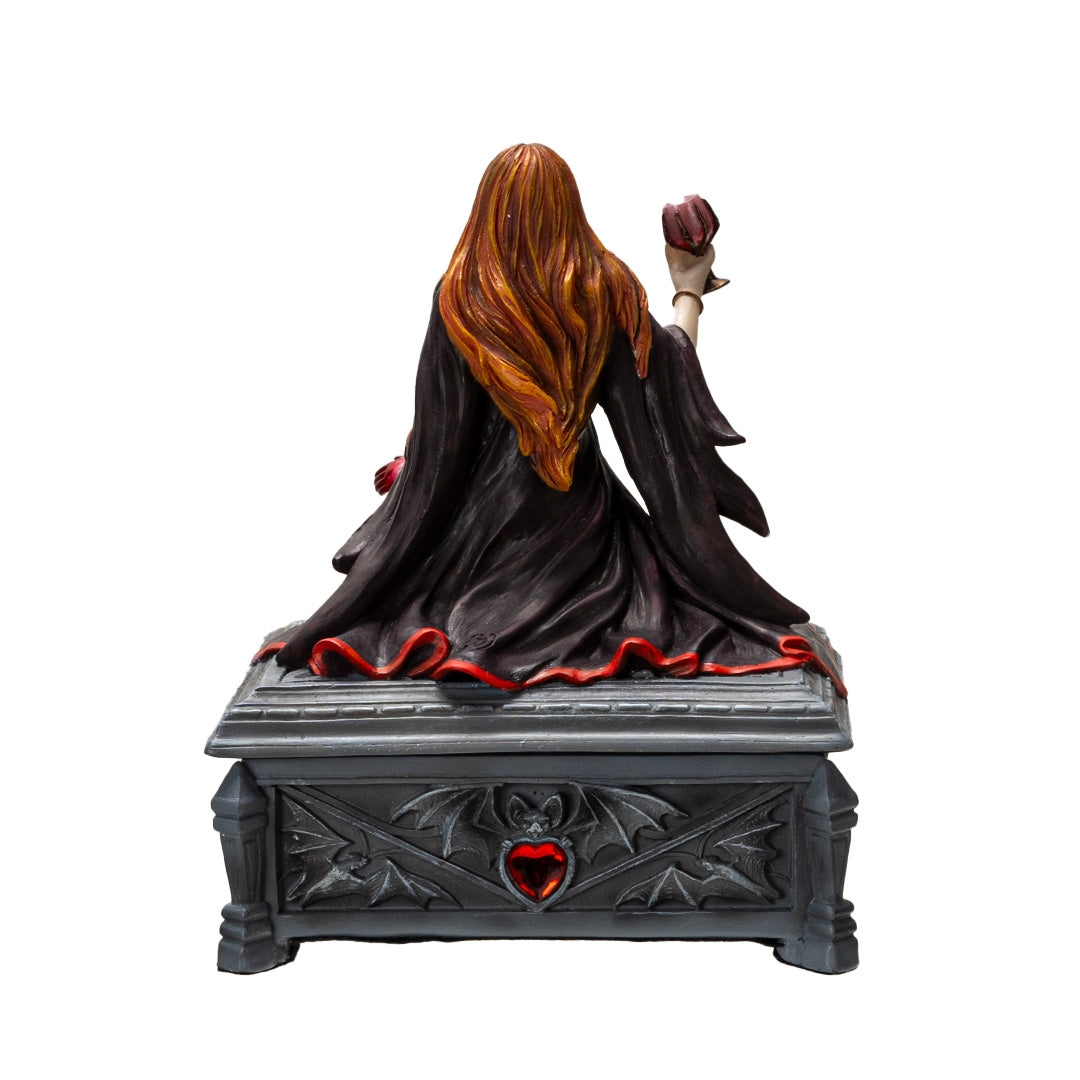 Trinket box, faux stone gray coffin with bat motif and red heart jewel. On lid is a vampire lady with 1 bloody hand and other holding a goblet, crimson and black skirt and top, auburn hair, fangs. Shown from the back
