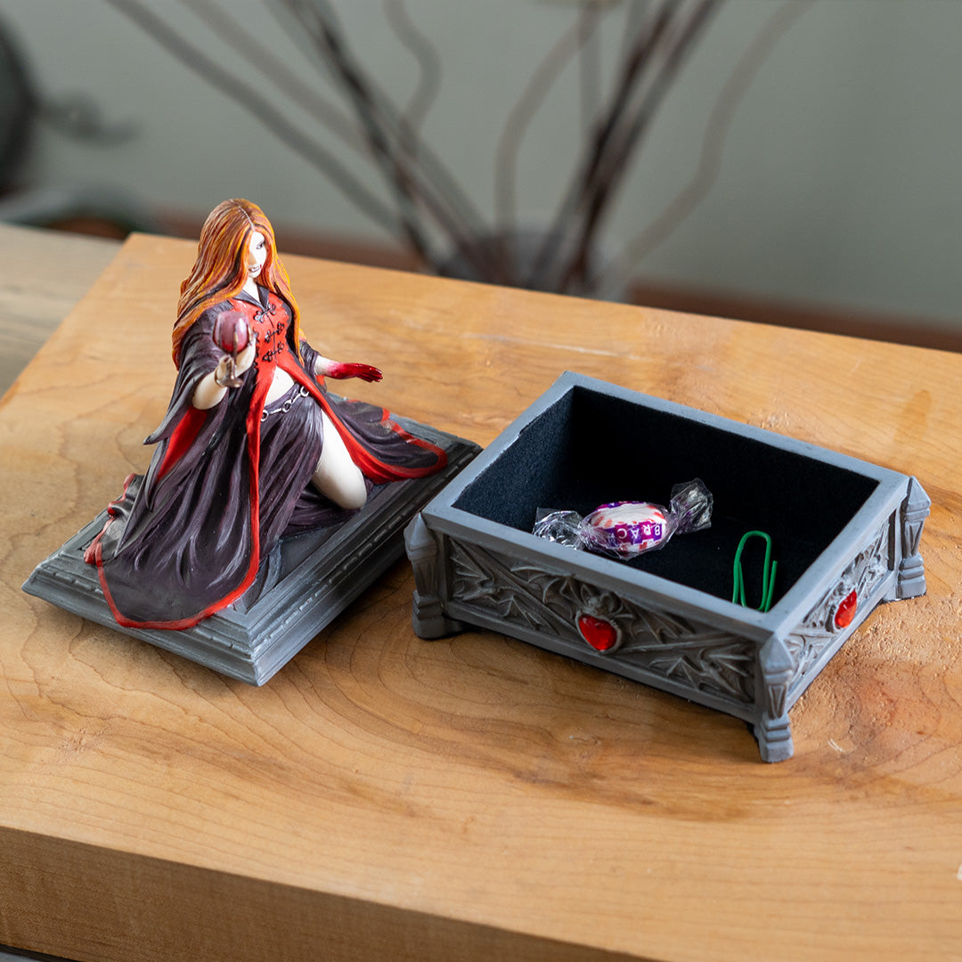 Trinket box, faux stone gray coffin with bat motif and red heart jewel. On lid is a vampire lady with 1 bloody hand and other holding a goblet, crimson and black skirt and top, auburn hair, fangs.