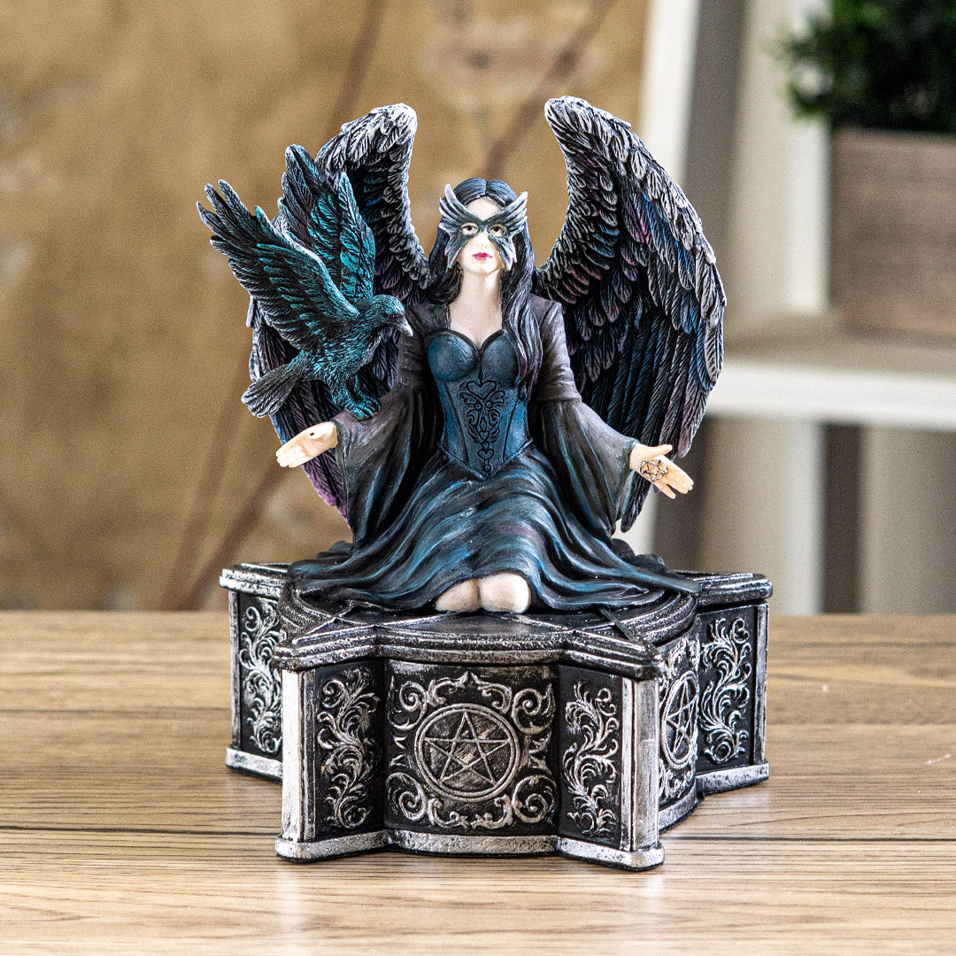 Trinket box, on the lid is a black feather winged angel with a raven on her arm, blue-black dress, black hair, mask. Base of box has pentacle designs